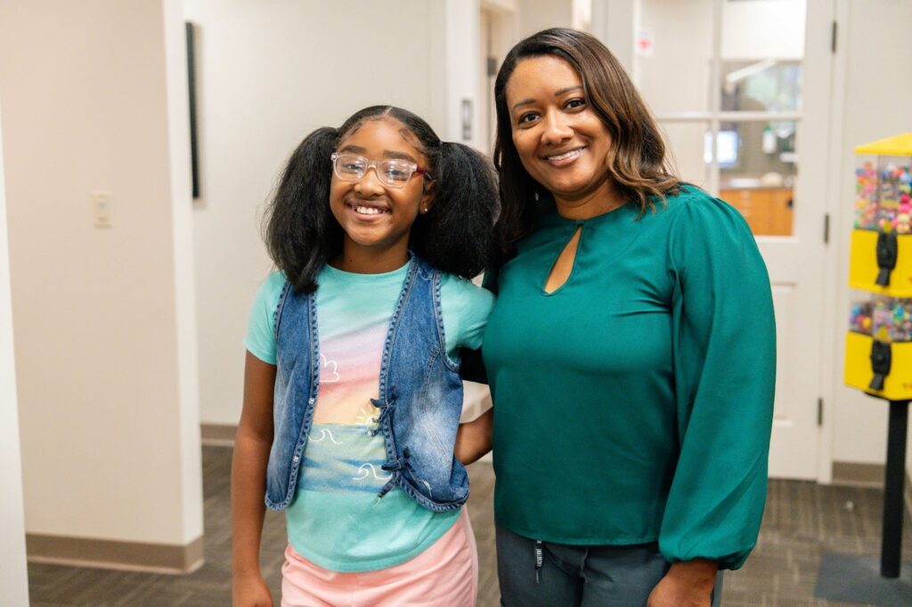 Smiling girl with glasses and pediatric dentist in a kid-friendly dental office, promoting children's dental care and comfort at Children's Dental Center.