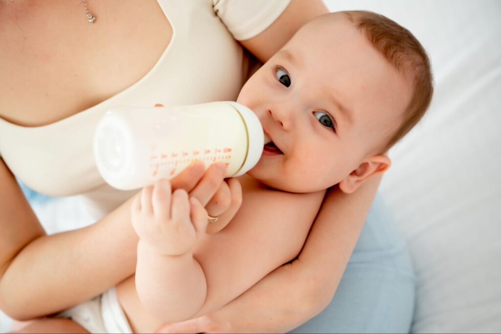 Baby drinking from a bottle in a caregiver's arms, illustrating baby bottle tooth decay concerns in pediatric dental health.